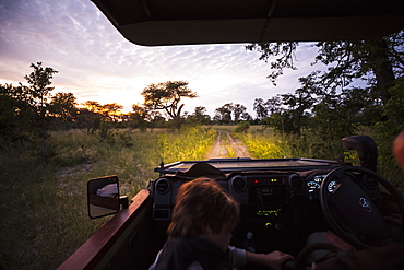 Motion blur, a safari vehicle driving on a dirt track with headlights on after sunset, Botswana