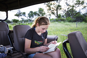 Thirteen year old girl writing in her journal seated in a jeep on safari, Botswana