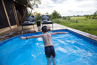 A six year old boy diving into a swimming pool at a tented camp, Botswana