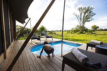 A boy in a swimming pool at a safari camp, looking out over the landscape, Botswana