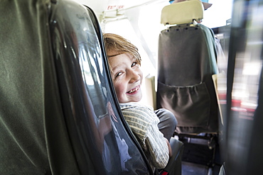 A smiling boy in a light aircraft seat, looking over his shoulder