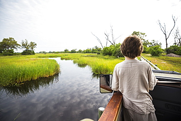 A six year old boy in a jeep on a bridge overlooking marshes and water, Botswana