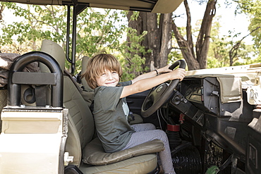 A five year old boy seated in the driving seat of a safari jeep pretending to drive, Okavango Delta, Botswana