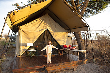 A five year old boy standing outside a tent arms outstretched, yawning yawning outside tent, Kalahari Desert, Makgadikgadi Salt Pans, Botswana