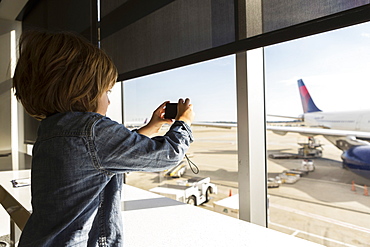 A five year old boy taking a photograph of airplane from an airport departure lounge