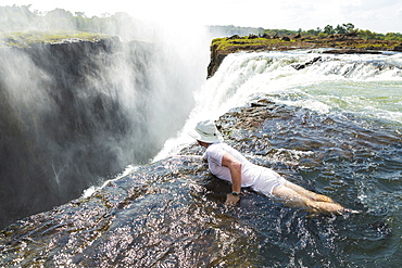 Man in the water at the Devils Pool on the edge of Victoria Falls, looking over the waterfall edge, Zambia