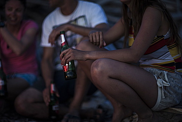 A group of young people gathered on a beach drinking beer