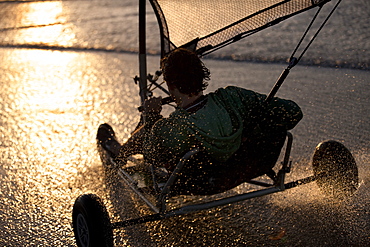 Rear view of person riding a sand yacht along a sandy beach at sunset