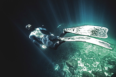 High angle underwater view of diver wearing wet suit and flippers, sunlight filtering through from above, United States of America