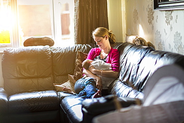 Mother relaxing with sleeping baby on sofa