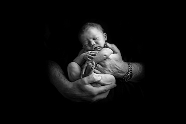 Sleeping newborn baby being held in hands of father