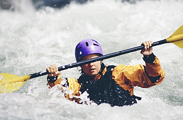 Female whitewater kayaker paddling rapids and surf on a fast flowing river