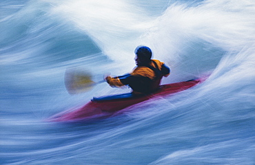 Long exposure of male whitewater kayaker paddling and surfing large rapids on a fast flowing river