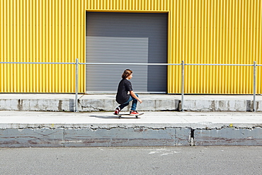 Teenage boy skateboarding in front of industrial warehouse loading zone