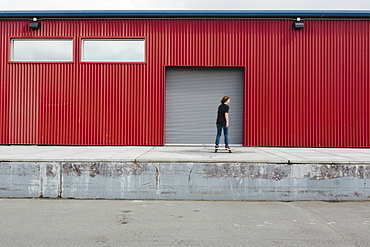 Teenage boy skateboarding in front of industrial warehouse loading zone