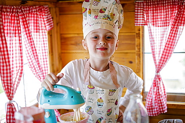 Portrait of young girl dressed in chef's outfit in wendy house pretending to cook in kitchen