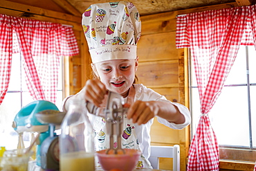 Young girl in wendy house using plastic whisk pretending to cook in kitchen