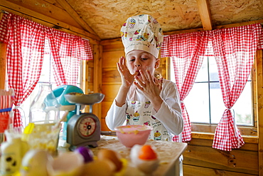 Young girl in wendy house liking fingers pretending to cook in kitchen