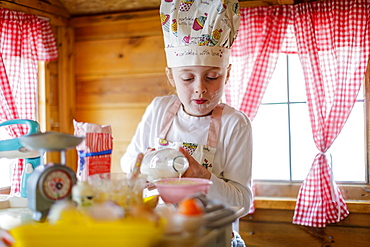 Young girl in wendy house pouring milk pretending to cook in kitchen