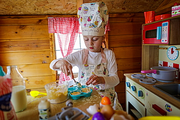 Young girl in wendy house pretending to cook in kitchen