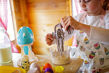 Young girl in wendy house using toy whisk pretending to cook in kitchen