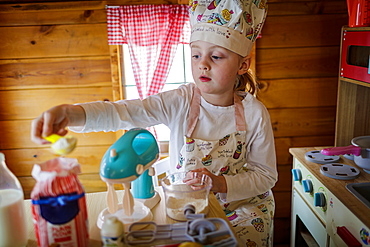 Young girl in wendy house pretending to cook in kitchen