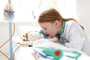 Young girl dressed as doctor pretending to treat patient in make-believe hospital bed