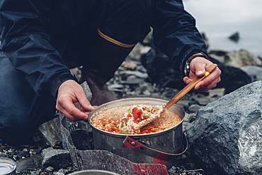 A wild camper stirring hot food in a pot cooking over a fire