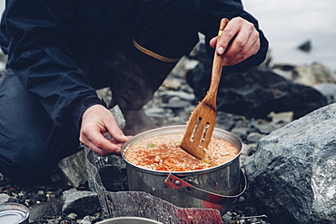 A wild camper stirring hot food in a pot cooking over a fire