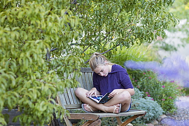 11 year old girl sitting on bench reading a book