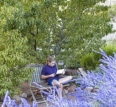 11 year old girl sitting on bench reading a book