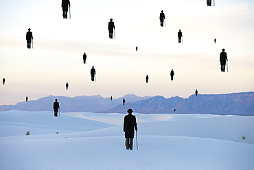 Men in bowler hats with umbrellas outline of figures floating above ground in a sand dune desert