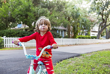 A five year old boy in a red shirt riding his bike on a quiet residential street