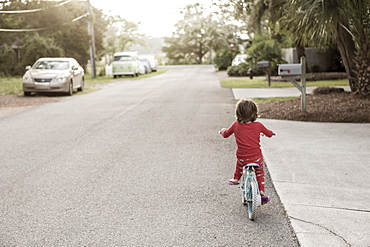 A five year old boy in a red shirt riding his bike on a quiet residential street