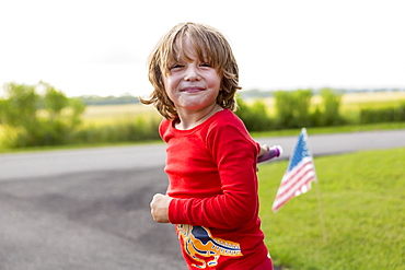 A five year old boy in a red shirt riding his bike on a quiet residential street