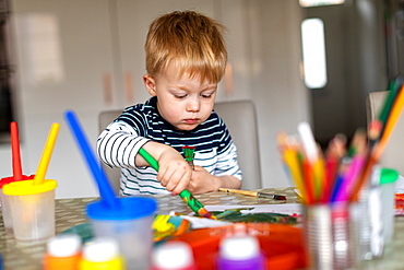 Three year old boy busy painting at home, with paint pots and brushes, Scotland, United Kingdom