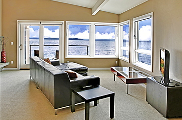 A living room in a waterfront house, with a large window and an ocean view, Washington, United States