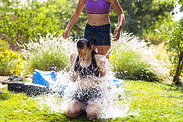 Two teenage girls wearing swimwear playing with water balloons in a garden, New Mexico, United States