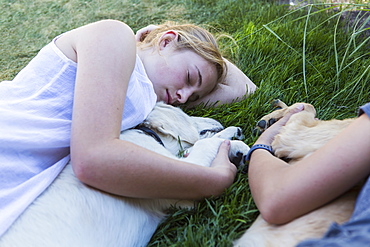 Two teenage girls lying on lawn, hugging their Golden Retriever dogs, New Mexico, United States