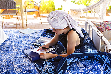 Teenage girl with hair wrapped in towel sitting on outdoor bed, doing homework, New Mexico, United States