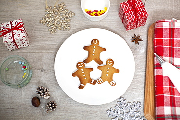 High angle close up of Christmas presents, decorations and Gingerbread Men on a white plate