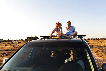 Teenage girl and her younger brother  on top of SUV on desert road, New Mexico, United States of America