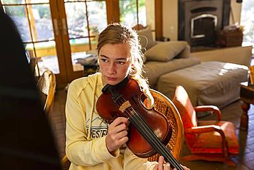 teenage girl plucking strings of her violin at home