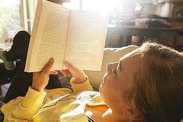 teenage girl reading book at home in early morning light