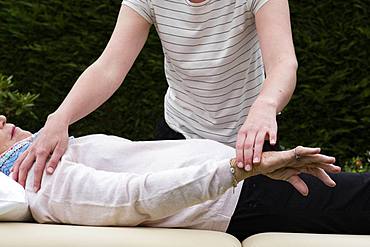 Reiki therapist with a client in a therapy session touching meridian points on the body