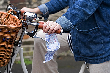 Close up of woman on bicycle, holding face mask, Oxfordshire, England, United Kingdom