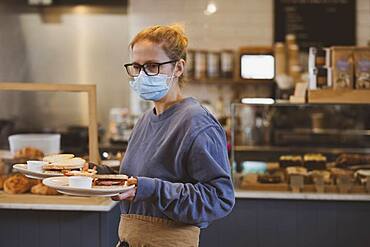 Waitress wearing face mask working in a cafe, carrying plates of food