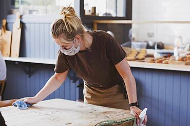 Waitress wearing face mask working in a cafe, wiping table