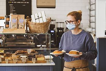 Waitress wearing face mask working in a cafe, carrying plates of food