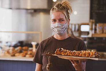 Waitress wearing face mask working in a cafe, carrying plate of food